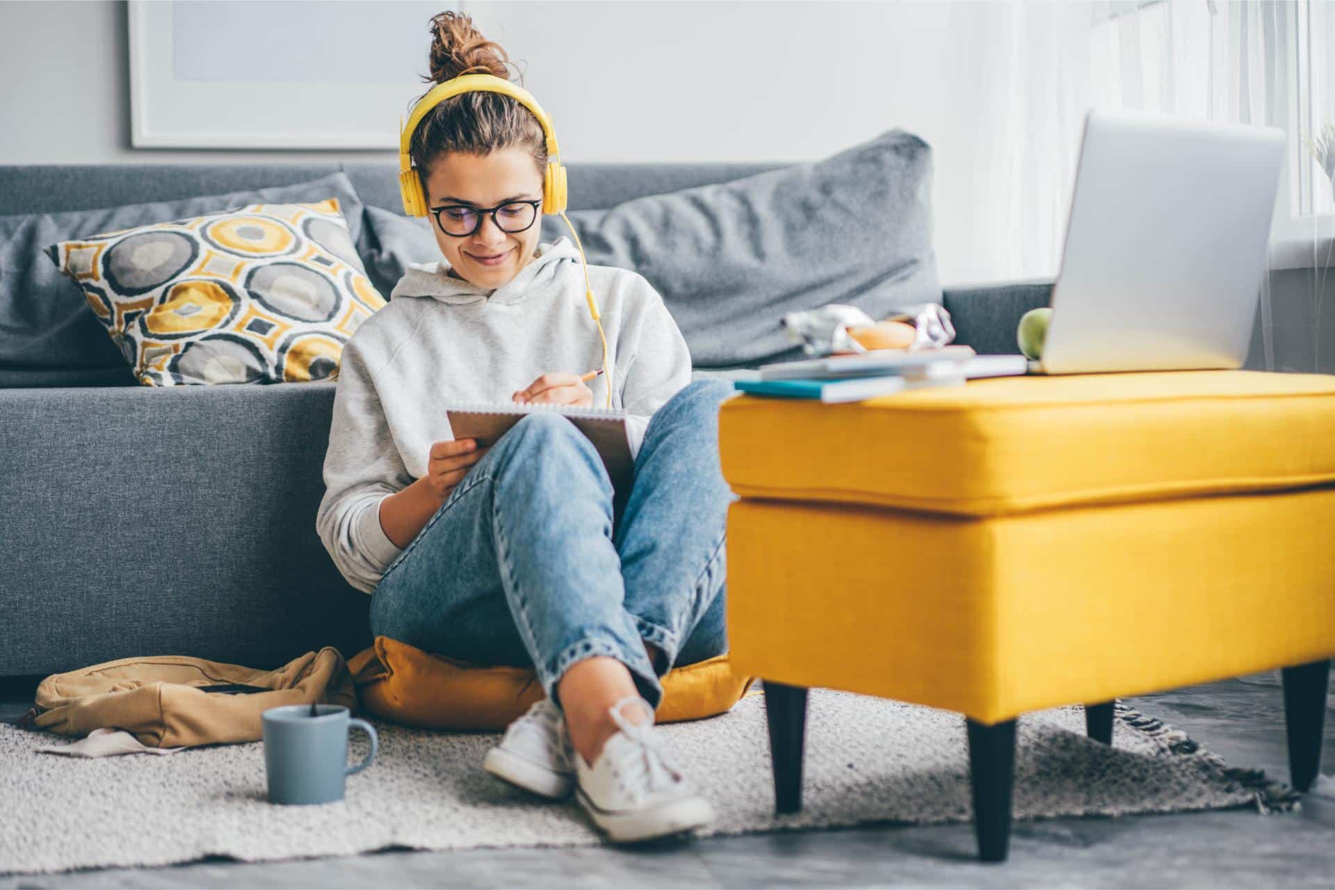 Sure! Based on your instructions, here's the rewritten description: Young woman with headphones writes in a notebook, sitting on the floor by a sofa and a laptop E-Liquid.